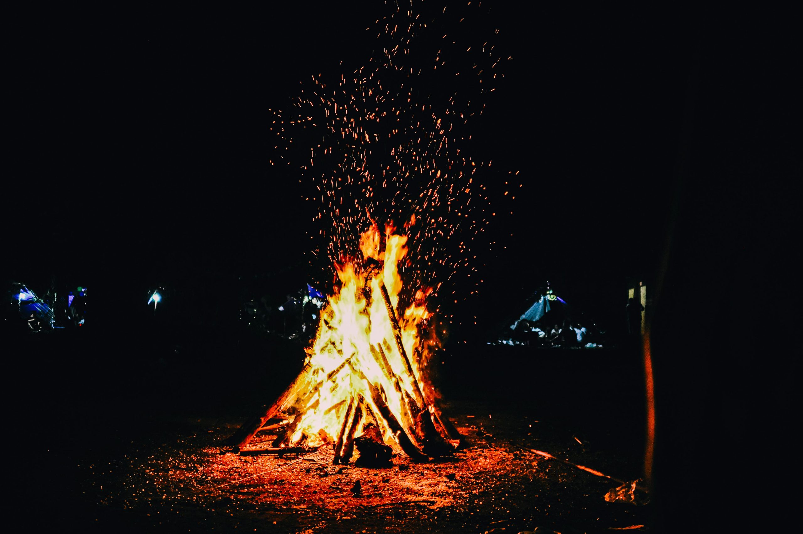 A blazing campfire outdoors at night sparks warmth and light.